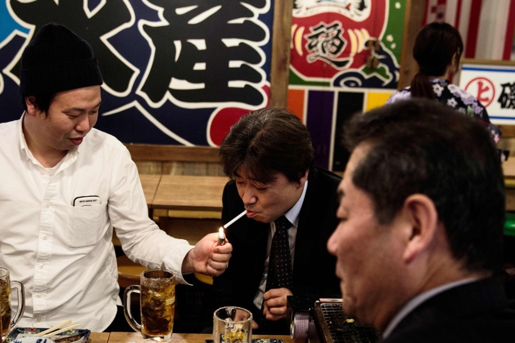 A man lights a cigarette for his friend in a Tokyo restaurant. Japan moved to install the strictest passive smoking laws ever. But resistance from some lawmakers stopped the zero tolerance approach from being introduced. Photo: AFP