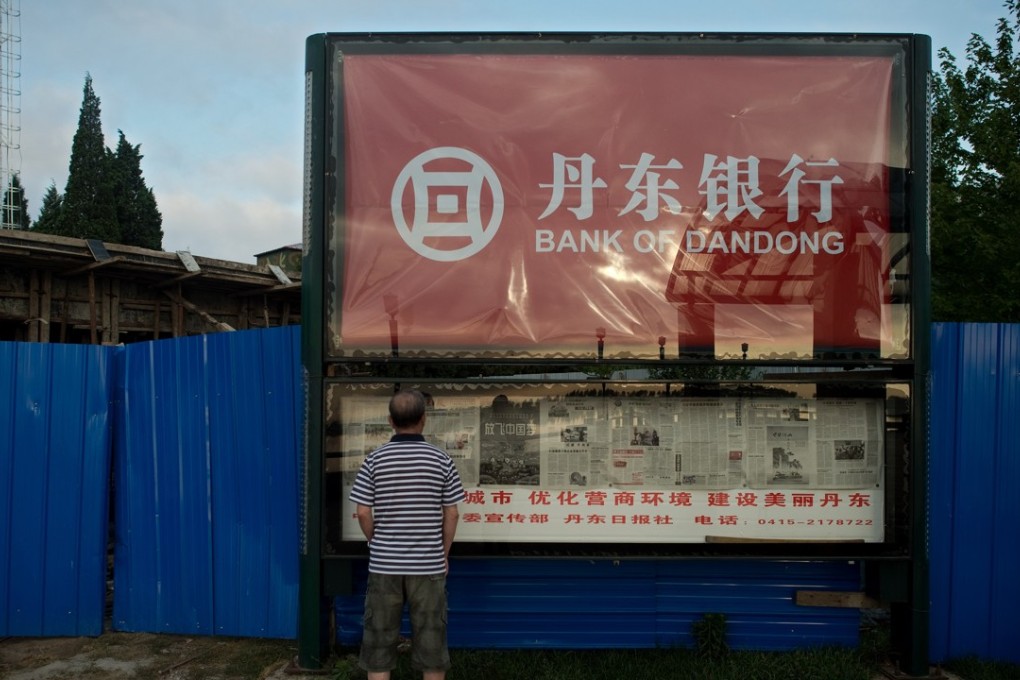 A man reads a newspaper displayed in a window billboard featuring a commercial for the "Bank of Dandong" near the Friendship bridge on the Yalu River connecting the North Korean town of Sinuiju and Dandong in Chinese border city of Dandong. Photo: AFP