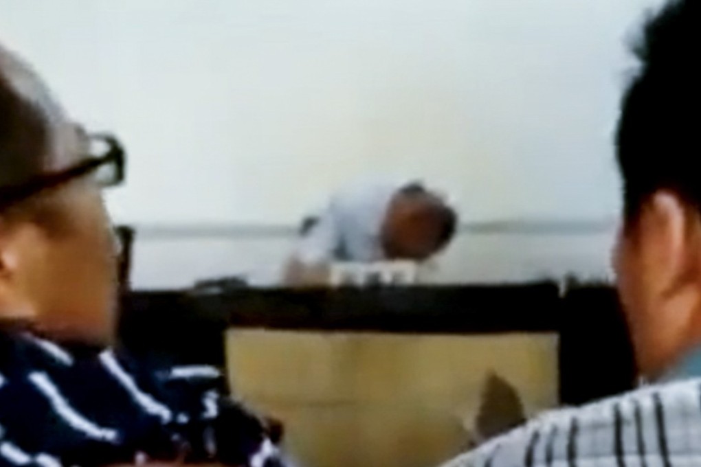 Two men look on as the inebriated judge takes a nap in his courtroom in central China. Local authorities said they have begun the process of dismissing him from the judicial system. Photo: Thepaper.cn