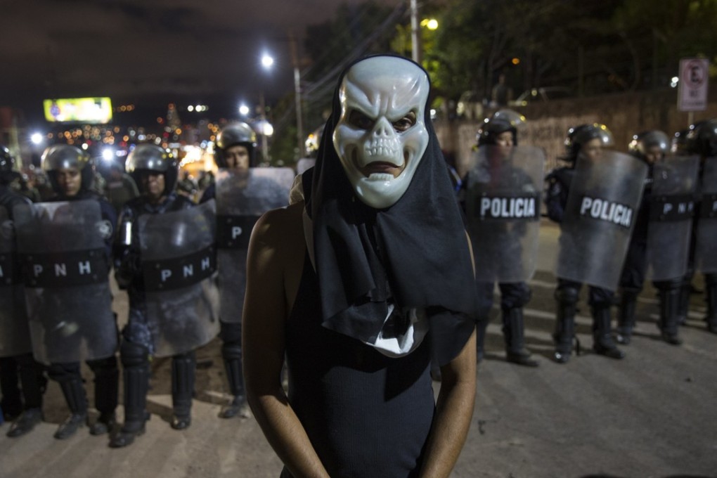 A masked supporter of presidential candidate Salvador Nasralla stands in front of police during a protest against the result of the presidential election. Photo: AP