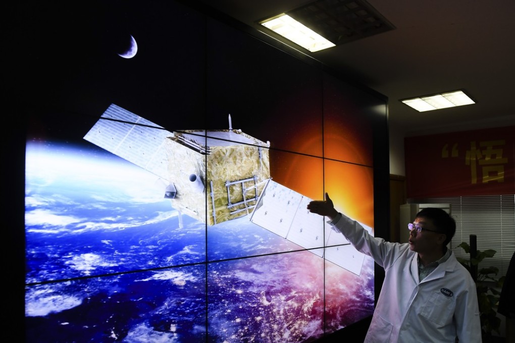 A scientist stands by an artist’s impression of the Chinese probe searching for dark matter. Photo: Xinhua