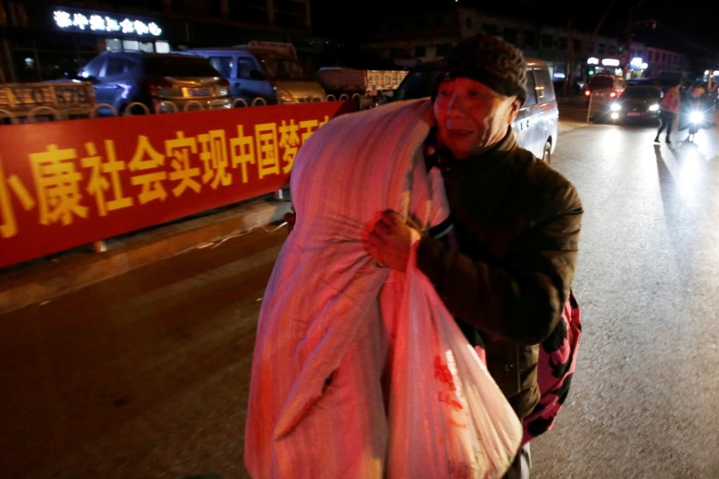 A migrant worker carries his bedding past a banner promoting the “Chinese dream” on a street in Beijing. Photo: Reuters