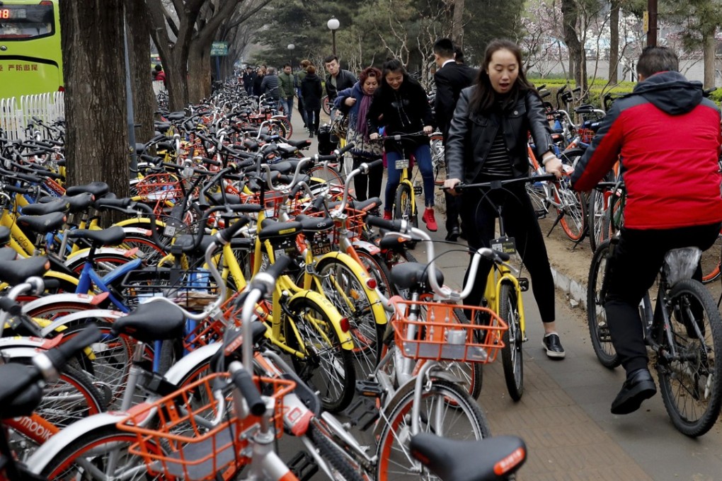 Residents ride bicycles through a sidewalk crowded with bicycles from the bike-sharing companies Ofo, Mobike and Bluegogo in Beijing. At its peak, about 100 companies were offering similar services in China. Photo: AP