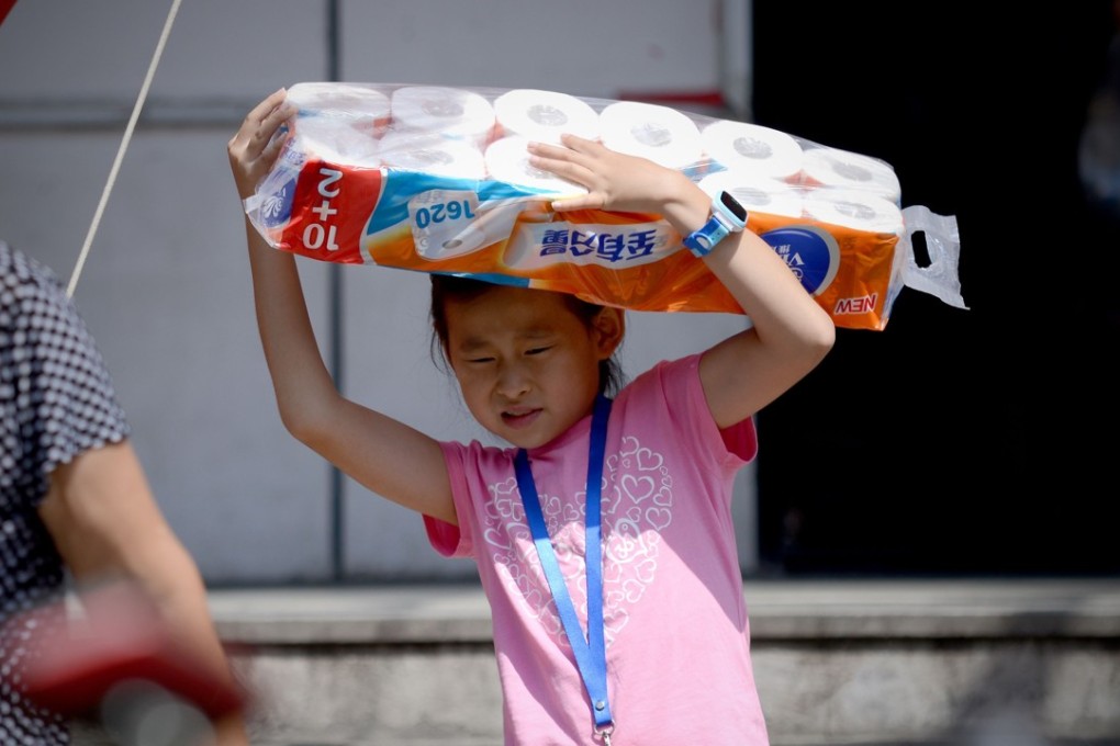 Stocking up: A girl walks out of a Beijing supermarket on August 9, 2016 with a bundle of toilet paper rolls. Photo: AFP