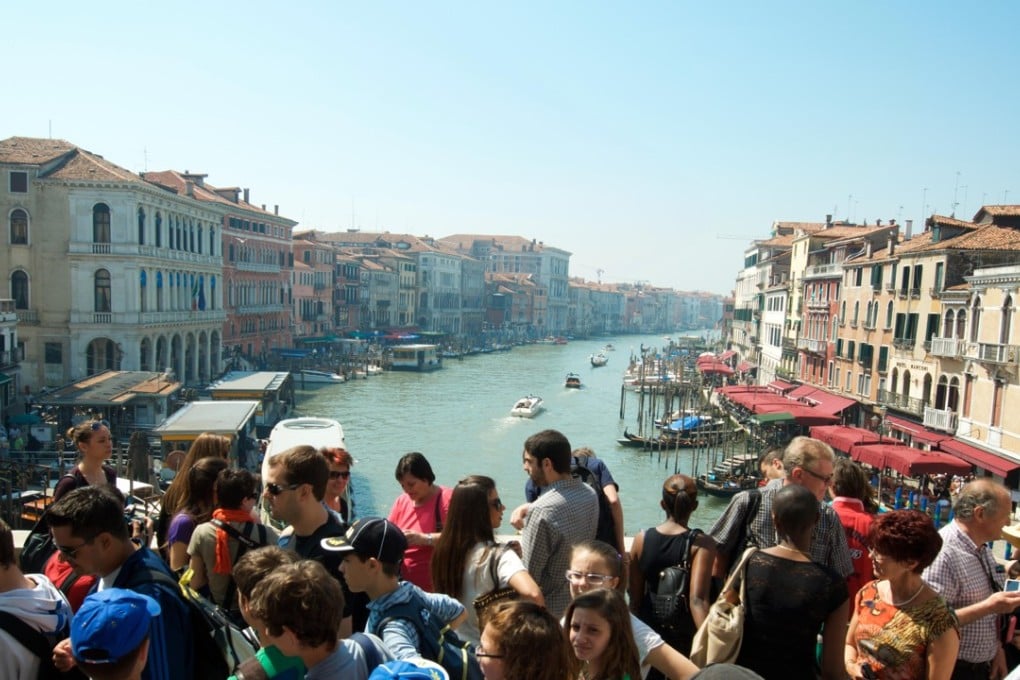 Crowds of tourists pass along the Rialto Bridge over the Grand Canal in Venice. Photo: Alamy
