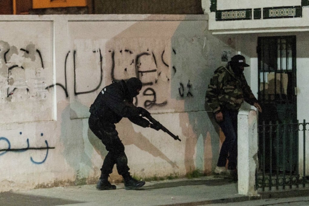 Mashed riot police hide behind a wall during anti-government protests in Tunis, Tunisia, on Wednesday. Photo: AP