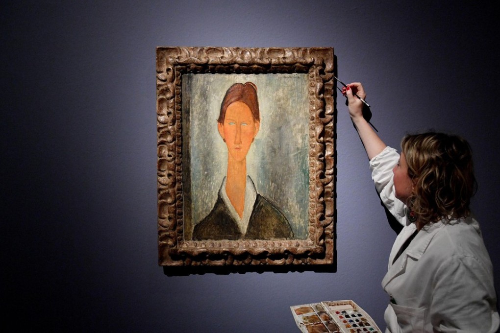 A woman touches up the fame of the painting “Portrait of Chaim Soutine”, attributed in the exhibit to Italian painter Amedeo Modigliani, on March 15, 2017, at a show in the Ducal Palace in Genoa, Italy. But a court-appointed expert has concluded that nearly all of the paintings in the show were fakes. Photo: AP