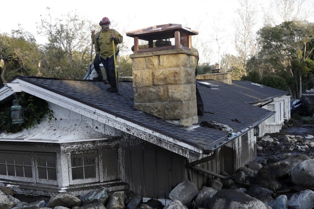 A firefighter stands on the roof of a house submerged in mud and rocks in Montecito, California. Photo: AP