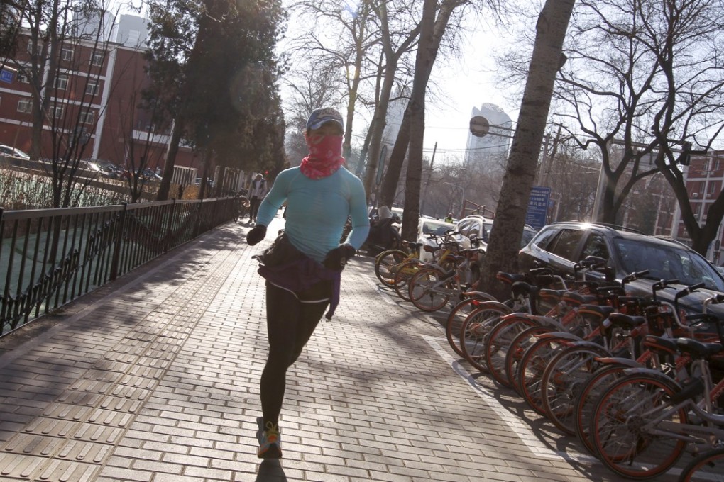 A woman uses a scarf to cover her face as she jogs through Beijing's central business district at noon on Friday. Authorities in the capital earlier issued the first smog alert of the year, saying air quality in the city was set to slump over the coming days. Photo: Simon Song