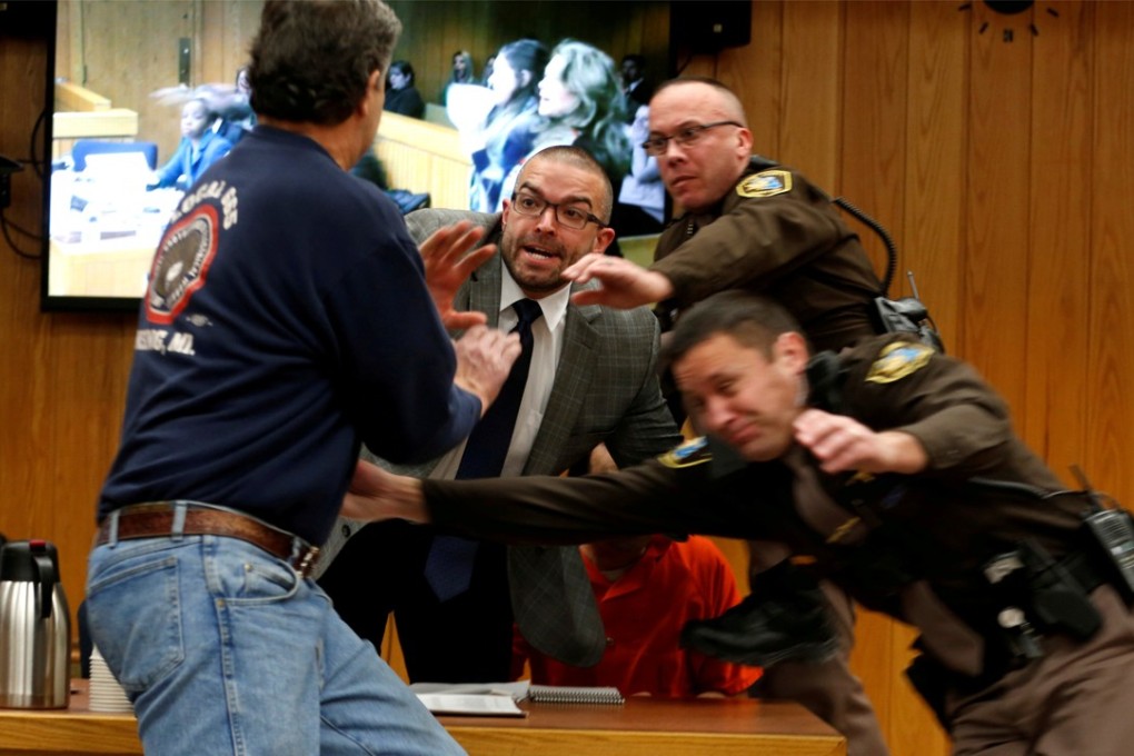 Randall Margraves (left), father of three victims of Larry Nassar, lunges at Nassar (bottom right, in orange jumpsuit behind guards) on Friday. The incident came during the third and final sentencing hearing for Nassar on sexual abuse charges. The charges in this case focus on his work with Twistars, an elite Michigan gymnastics club. Photo: Photo: Reuters