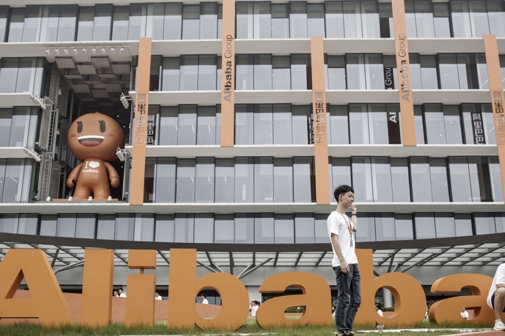 Employees and visitors pose for a photograph in front of signage for Alibaba Group Holding Ltd. at the company's headquarters in Hangzhou, China. Photo: Bloomberg