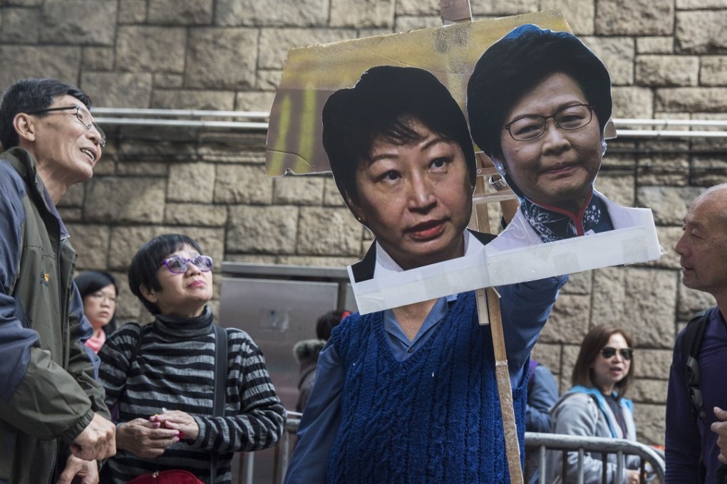 A protester (C) holds a placard of Hong Kong's justice secretary Teresa Cheng and Hong Kong’s chief executive Carrie Lam during a march on February 11, 2018, calling for Cheng to step down over illegal structures that were found at the homes she owns. Photo: AFP