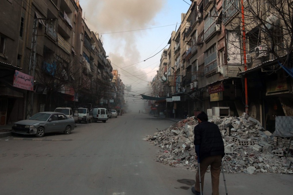 A Syrian man on crutches walks down a street as smoke billows in the rebel-held town of Douma, in the besieged Eastern Ghouta region on the outskirts of the capital Damascus, following air strikes by regime forces on the area on Friday. Photo: AFP