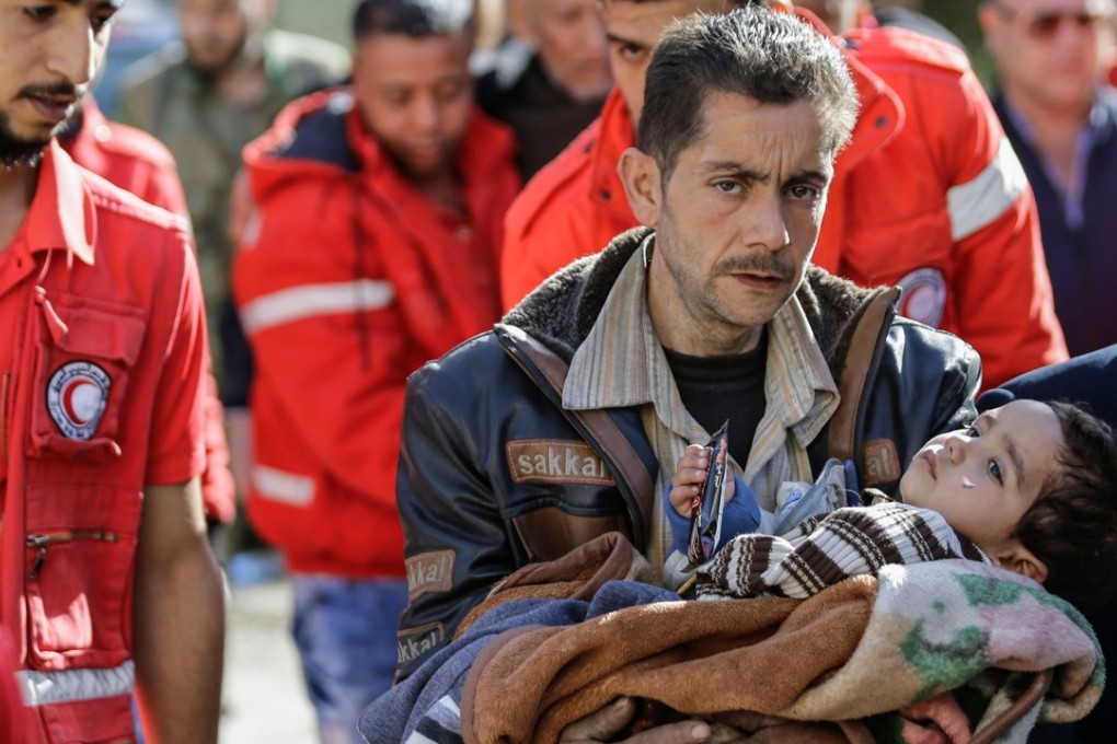 A Syrian man carries a child after evacuating from the Eastern Ghouta enclave into the government side of the Wafideen checkpoint on the outskirts of the Syrian capital Damascus on March 14, 2018. / AFP PHOTO / LOUAI BESHARA