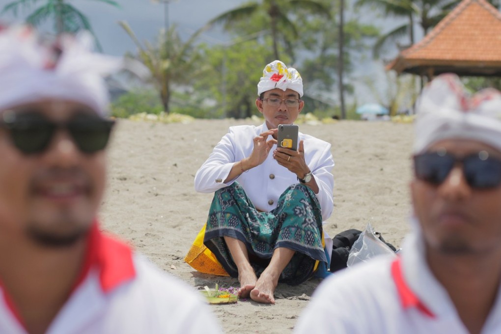 A Balinese Hindu uses his mobile phone on a beach during a Melasti purification ceremony, ahead of the holy day Nyepi, in Gianyar, Bali. Photo: Reuters