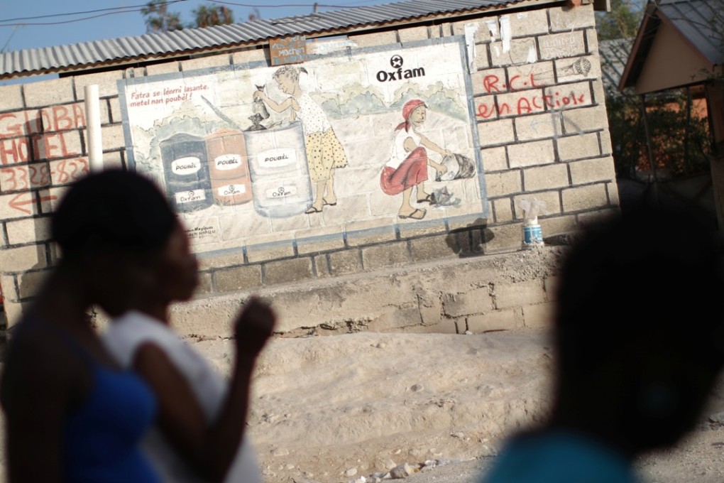 Women walk past an Oxfam sign in Corail, a camp for displaced people of the 2010 earthquake, on the outskirts of Port-au-Prince, Haiti. Oxfam is facing fresh allegations of sexual misconduct by staff in Haiti. Photo: Reuters