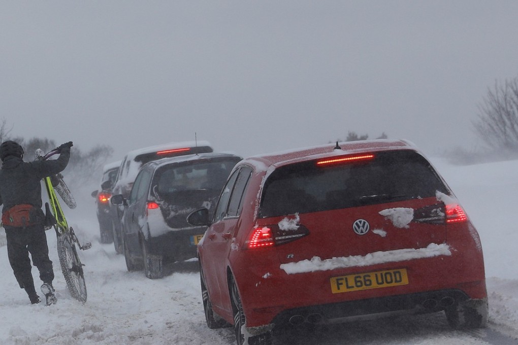 A man pushes his bicycle past cars stuck in the snow in Coalville, Britain on March 18, 2018. Heavy snow continued to hammer the UK. Photo: Reuters