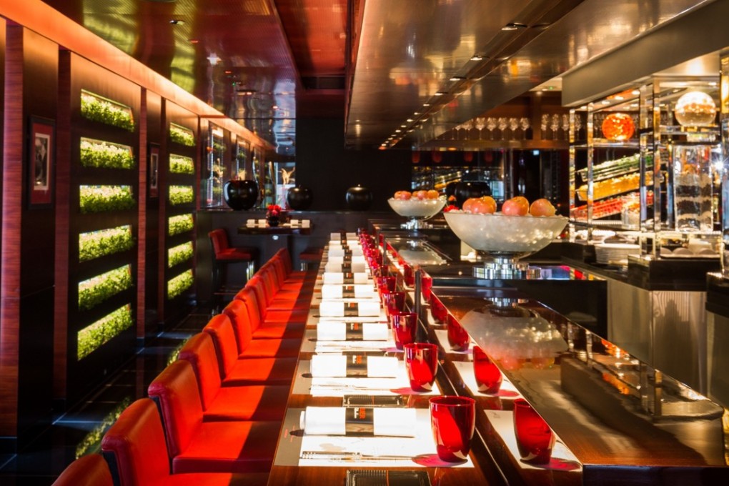 L’Atelier de Joël Robuchon has a section with tall vibrant red seats around an open kitchen.