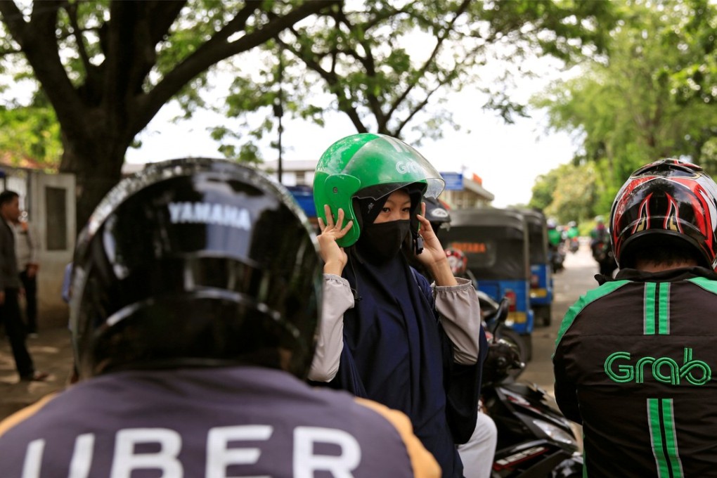 A passenger of Grab bike fixes her helmet next to Uber driver at Manggarai railway station in Jakarta, Indonesia, March 26, 2018. REUTERS/Beawiharta