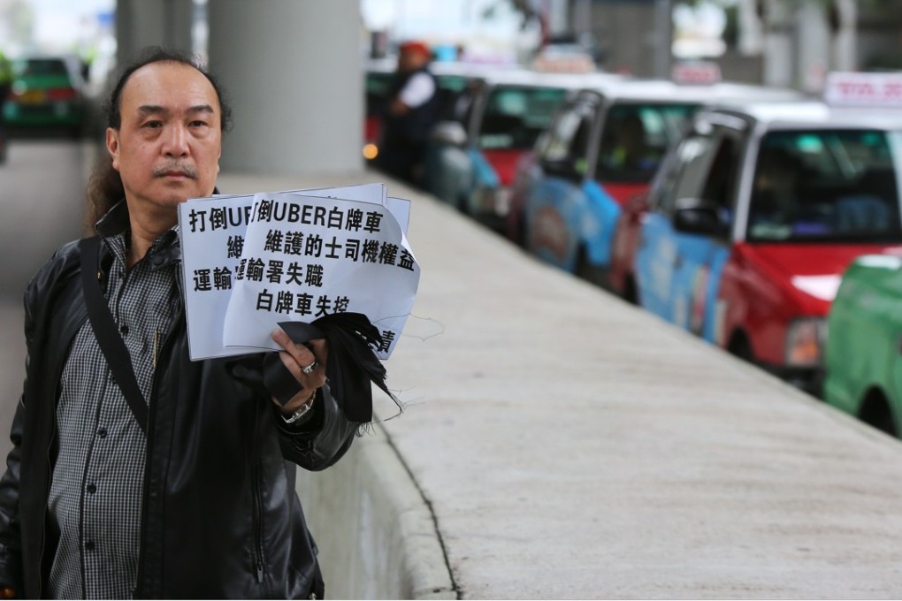 A taxi driver holds up a sign calling on the government to crack down on Uber during a slow-drive protest outside the government headquarters in Tamar on March 15. Photo: Xiaomei Chen