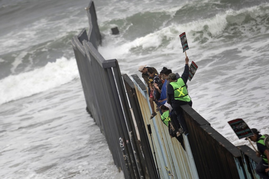 Central American migrants traveling with a caravan sit momentarily on top of the border wall between Tijuana, Mexico (left) and San Diego (right) on Sunday. US immigration lawyers are telling migrants in a caravan of asylum-seekers that traveled through Mexicothat they face possible separation from their children and detention for many months as they are processed. They say they want to prepare them for the worst possible outcome. Photo: AP