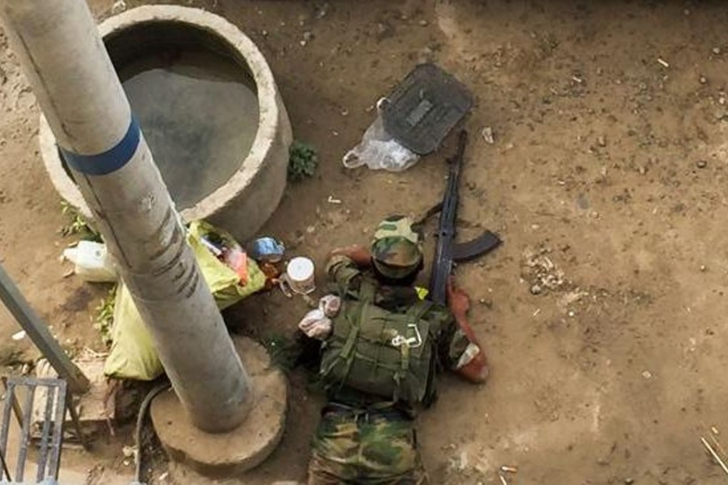 An alleged Ta'ang National Liberation Army (TNLA) soldier hides behind a car during clashes with Myanmar’s military in Muse on May 12, 2018. Photo: AFP
