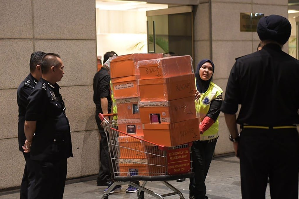 A policewoman wheels a shopping trolley full of boxes with valuables removed during a raid in Kuala Lumpur on three luxury flats owned by former prime minister Najib Razak’s family. Photo: AFP/The Straits Times