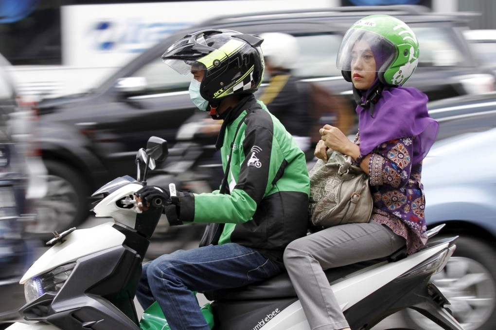 A woman rides on the back of a motorbike, part of the Go-Jek ride-hailing service, on a busy street in central Jakarta, Indonesia. Photo: Reuters