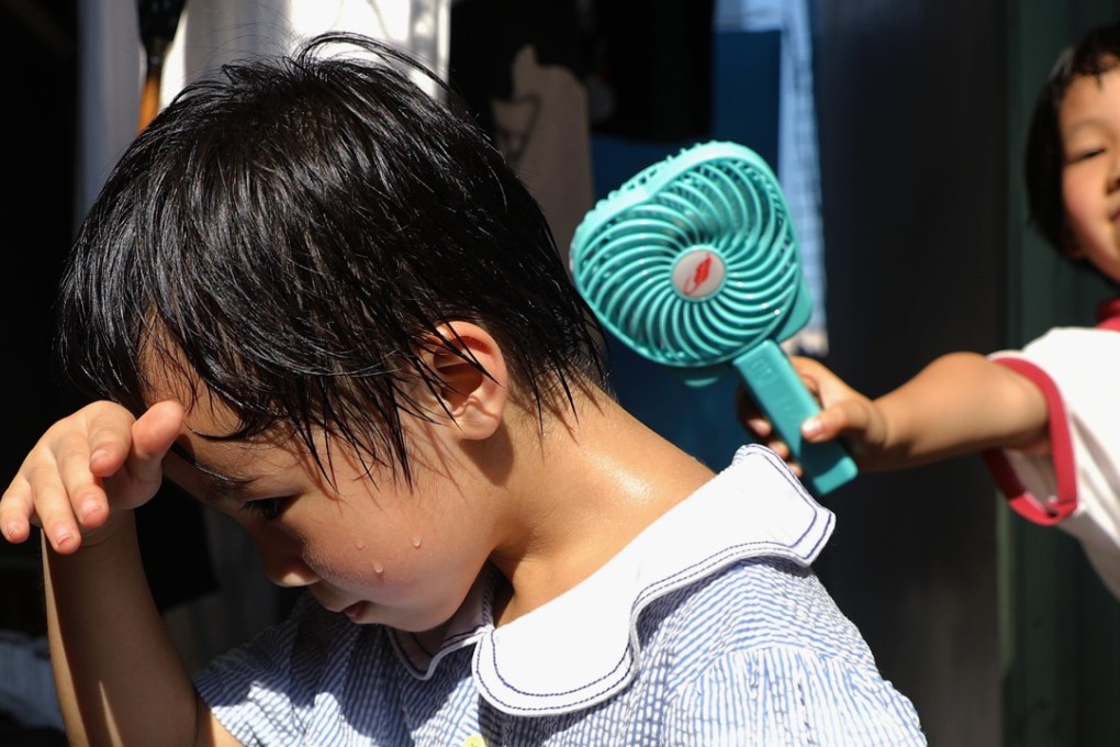 Chiu Ka-wai (back), 6, holds a mini fan for her cousin Wu Pik-yee, 5.5 years-old (front), outside the illegal structure they live in. Photo: Sam Tsang