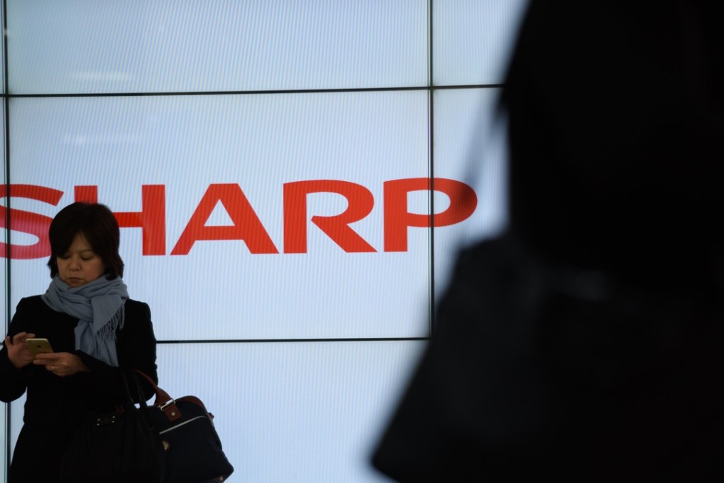 A woman uses her mobile phone in front of a Sharp Corp. liquid-crystal display in Tokyo, Japan. Photo: Bloomberg