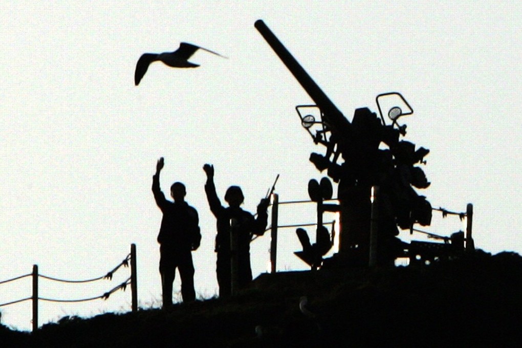 Two South Korean armed police officers, standing guard on the Dokdo islets, wave toward tourists aboard a boat. Photo: Reuters