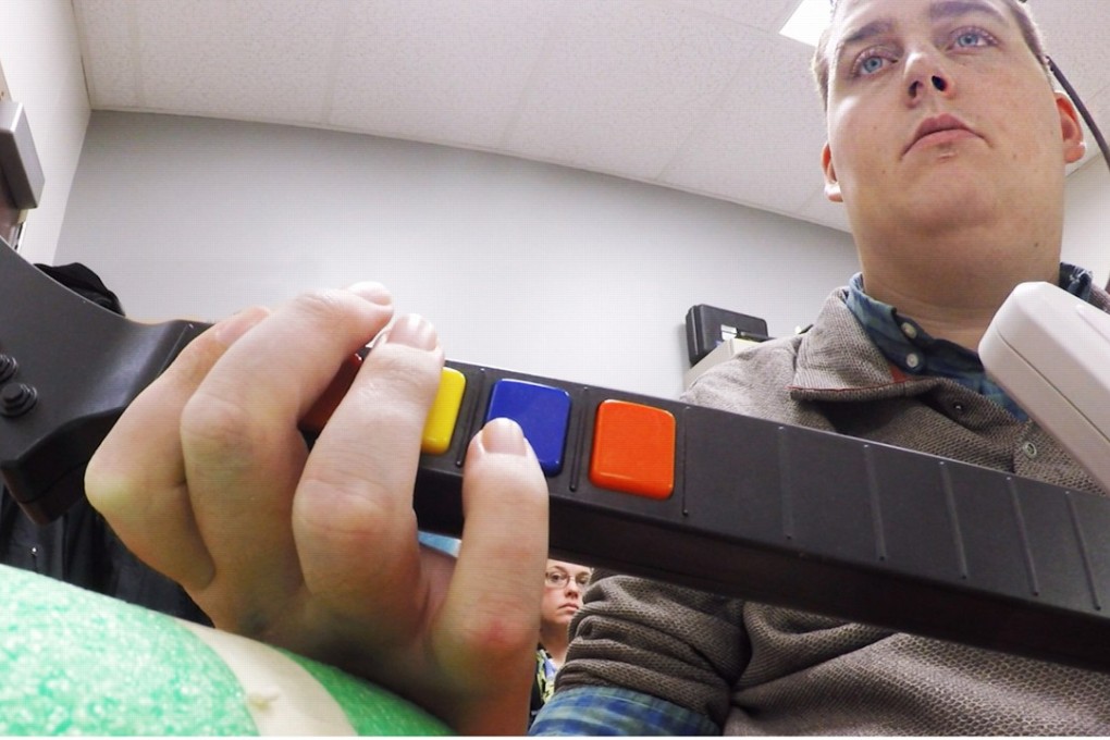 Ian Burkhart plays a guitar video game as part of a study with neural bypass technology. A computer chip in Burkhart`s brain reads his thoughts, decodes them, then sends signals to a sleeve on his arm that allows him to move his hand. Photo: Ohio State University/Batelle Memorial Institute