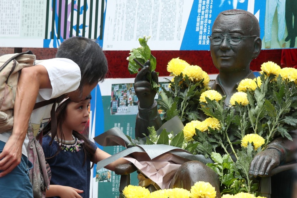 A child places a flower on a statue of Liu Xiaobo outside Times Square in Causeway Bay on June 12. Activists who set up a stall to commemorate the late Nobel Peace Prize winner were asked to vacate the area on June 19. Photo: K.Y. Cheng