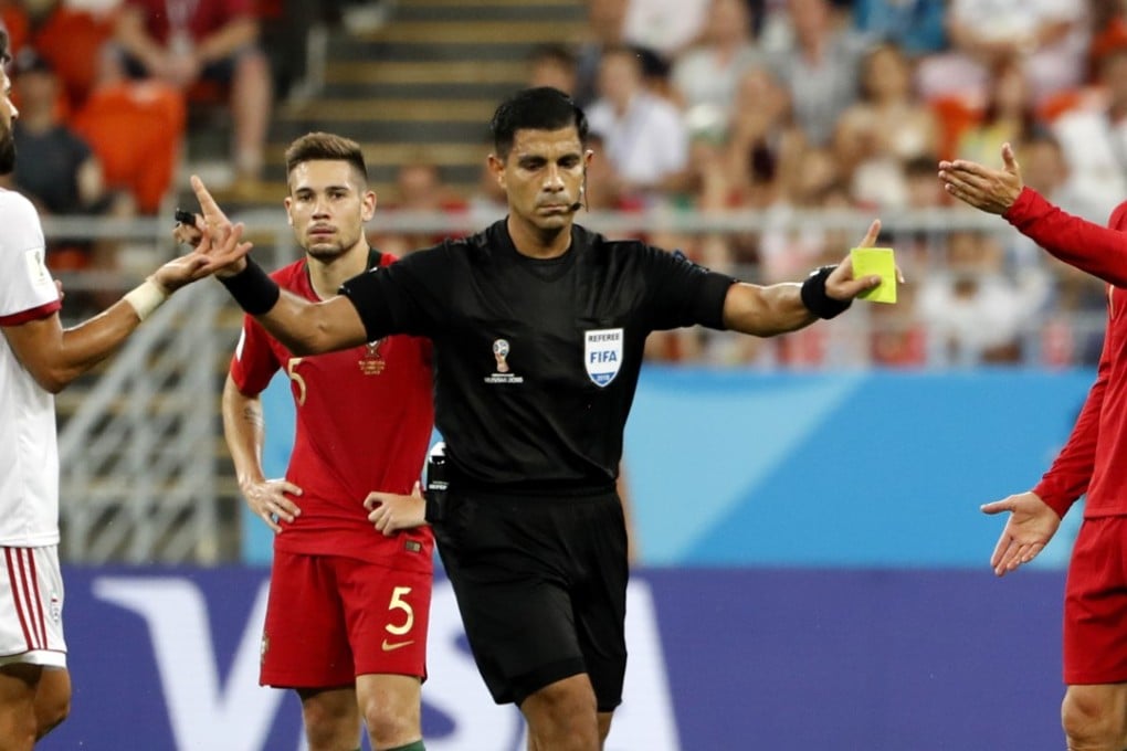 Cristiano Ronaldo (right) receives a yellow card from referee Enrique Caceres, but Iran’s players argue it should be red. Photo: EPA