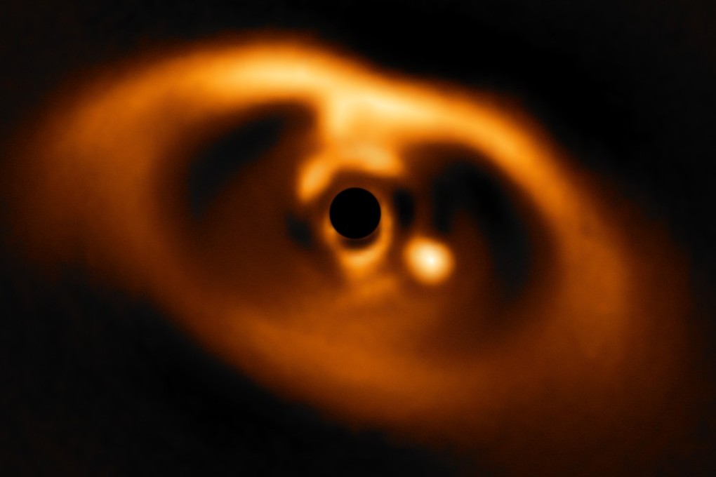 This image from the European Southern Observatory's Very Large Telescope is the first clear image of a planet caught in the act of formation, around the dwarf star PDS 70. The planet is visible as a bright point to the right of the centre of the image, blacked out by the round filter used to block the blinding light of the central star. Photo: A. Muller et al/ESO