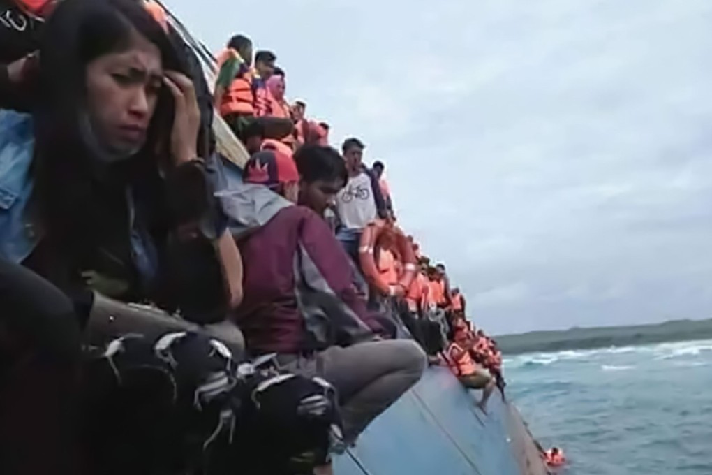 Passengers are perched on the listing vessel as others descend into the heavy seas using ropes hung over its side. Photo: AFP