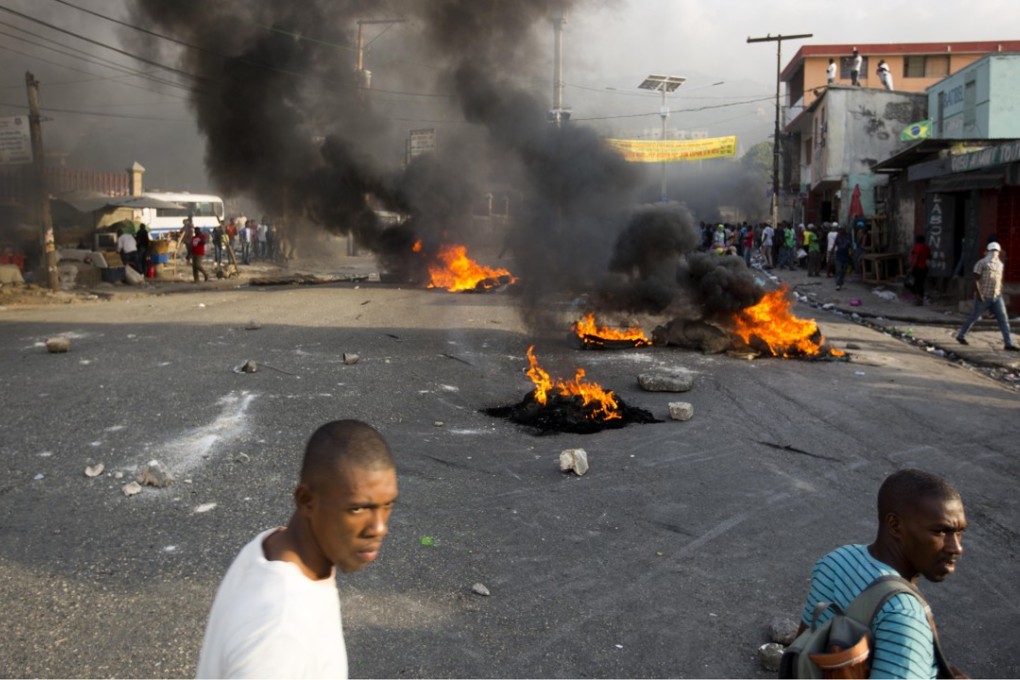 People walk past a barricade during a protest over the cost of fuel in Port-au-Prince, Haiti on Friday, July 6, 2018. Photo: AP
