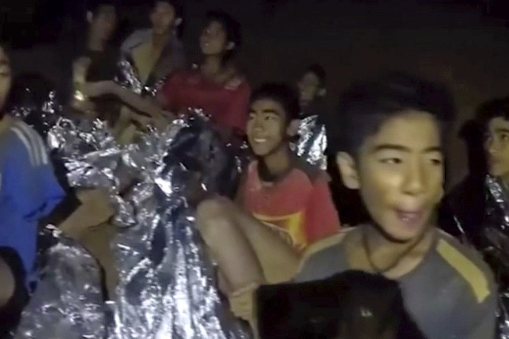 In this July 3, 2018, image taken from video provided by the Royal Thai Navy Facebook Page, Thai boy smiles as Thai Navy Seal medic help injured children inside a cave in Mae Sai, northern Thailand. The Thai soccer teammates stranded more than a week in the partly flooded cave said they were healthy on a video released Wednesday, as heavy rains forecast for later this week could complicate plans to safely extract them. (Royal Thai Navy Facebook Page via AP)