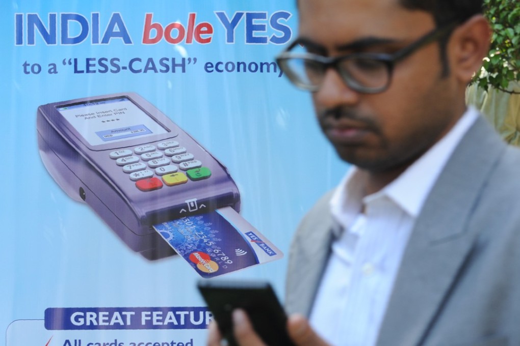 An Indian bank teller checks his phone as he walks past a poster advertising electronic payments in Mumbai, India. Photo: AFP