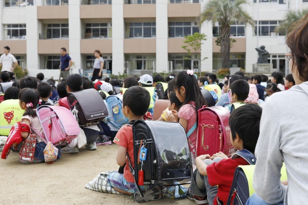School children take shelter at schoolyard in Ikeda, Osaka, following an earthquake Monday, June 18, 2018. A strong earthquake has shaken the city of Osaka in western Japan. There are reports of scattered damage including broken glass and concrete. (Takaki Yajima/Kyodo News via AP)