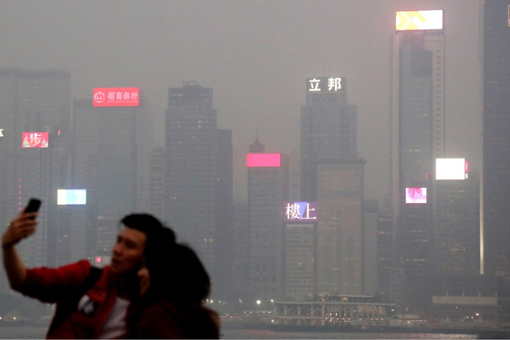 A couple take a picture by the water in Tsim Sha Tsui, with the Victoria Harbour skyline under heavy smog in the background. Photo: K.Y. Cheng