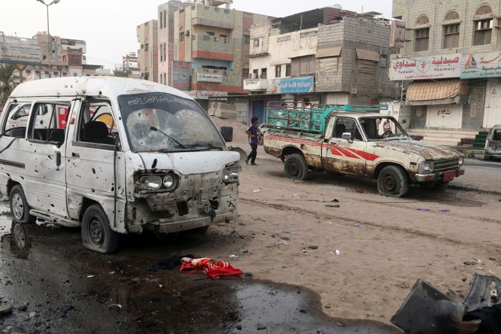 People walk past damaged cars at the entrance of Al-Thawra hospital. Photo: AFP
