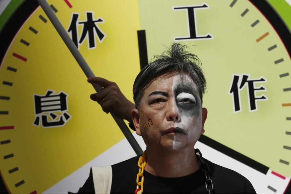 A protester with half his face painted as a zombie poses in front of a mock clock divided into “rest” and “work”, as part of a march to mark Labour Day in Hong Kong in 2015. Photo: AP