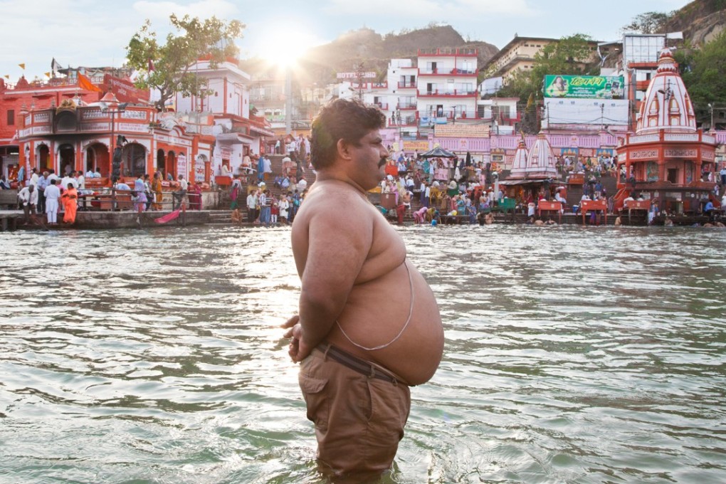 An overweight man stands in the River Ganges in India. While obesity can cause many diseases, it can be seen as a chronic illness in itself. Photo: Alamy