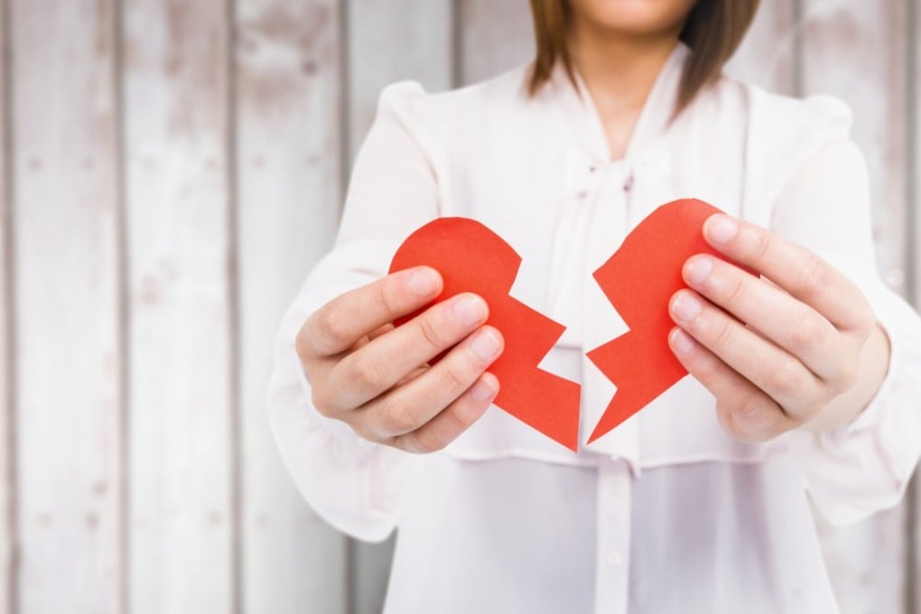 Mid-section of woman holding a broken heart against wooden background. Photo: Shutterstock