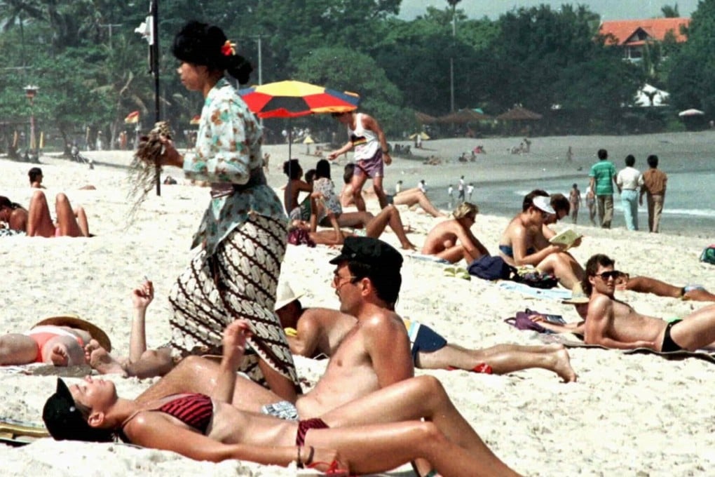 A Balinese woman in traditional dress walks past foreign tourists sunbathing on Kuta Beach on the Indonesian island of Bali in 1996 when mass tourism was in full swing. Picture: Reuters