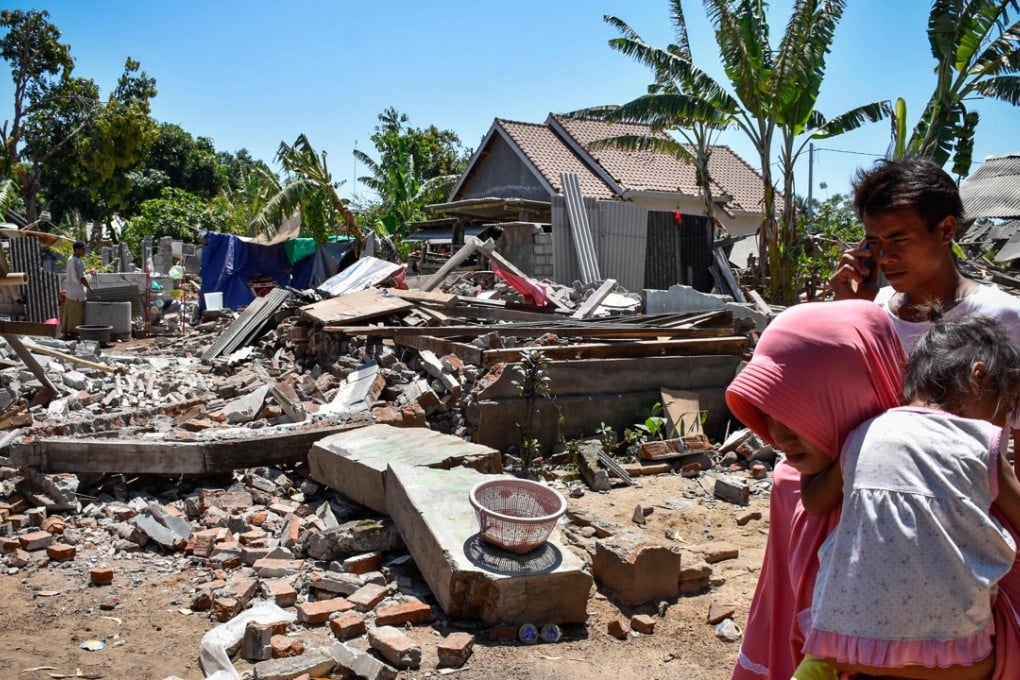 A woman carries her child as they make their way pass collapsed homes in the village of Sugar on Indonesia's Lombok island. Photo: AFP