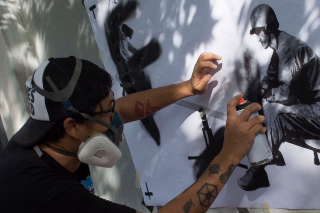 Thai artist “Headache Stencil” spray-paints graffiti on a fence in Bangkok. Photo: AFP