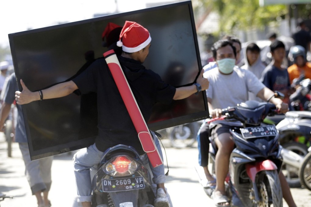 A man carries a big-screen TV taken from a tsunami devastated shopping centre in Palu. Photo: EPA
