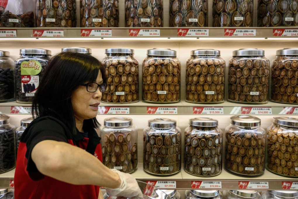 An employee holds a jar of dried products as she walks past shelves of jars containing dried abalone and other seafood goods in a shop in Hong Kong. Demand for abalone by Chinese gangs has caused South Africa's stocks of the marine molluscs to be depleted at a record rate. Photo: AFP